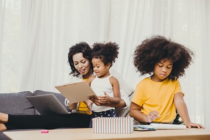 Woman sitting on couch helping two children with school work. 