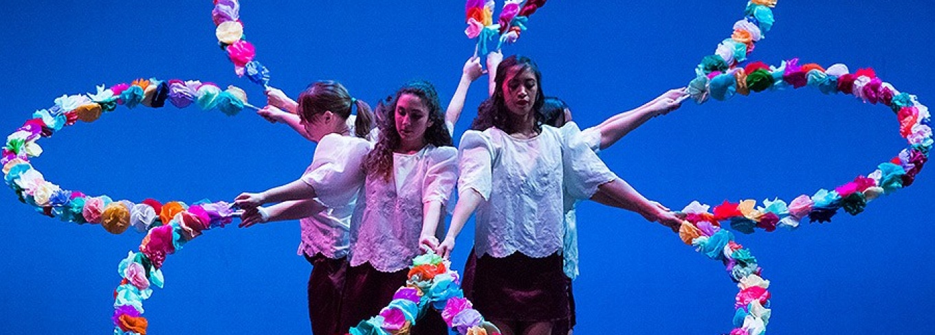Four women stand in the middle of giant fake flower on a stage.