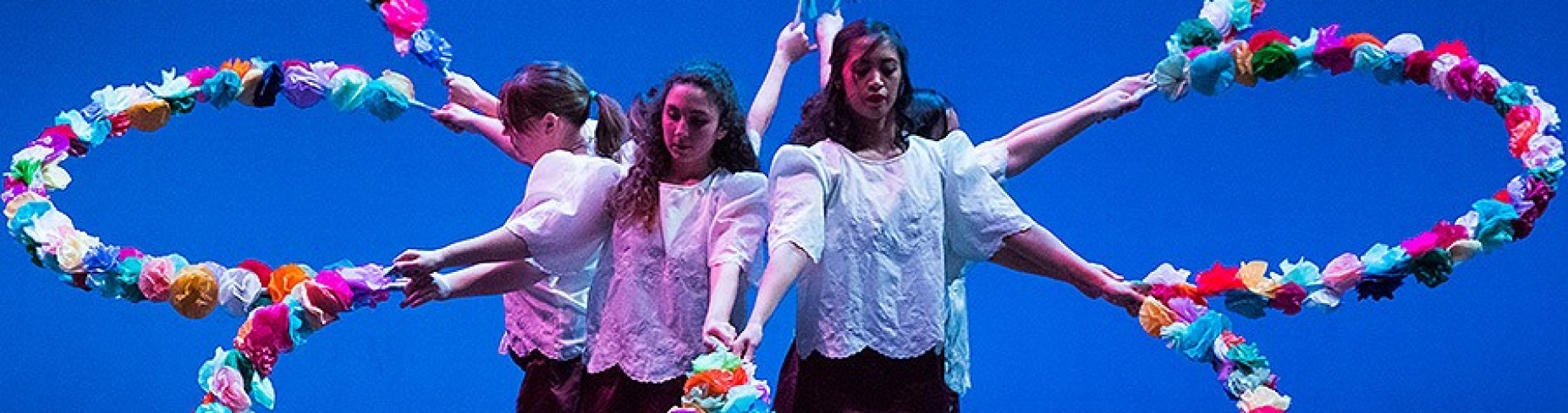 Four women stand in the middle of giant fake flower on a stage. 