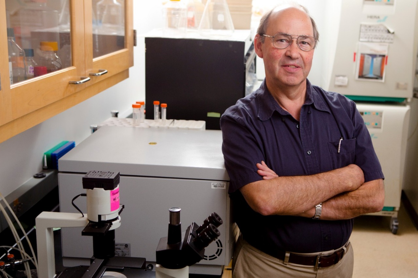 Michael Russell standing, arms folded, in lab. 