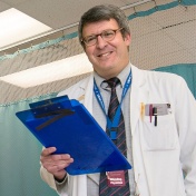 Gil Wolfe in white coat, holding clipboard. 