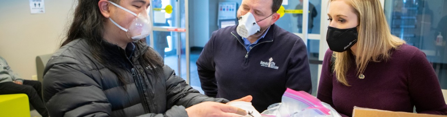 L to R: UB dental student Philip Sales shows the clear, reusable face mask produced by UB to Michael O'Hara and Heather Mattiuzzo of the Buffalo City Mission.