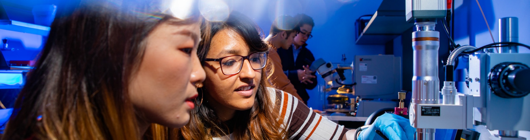 Two female students working with a microscope type device in Huamin Li's lab. 