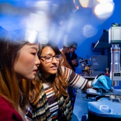 Two female students working with a microscope type device in Huamin Li's lab. 