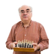 Ken Regan stands holding a chess board. 