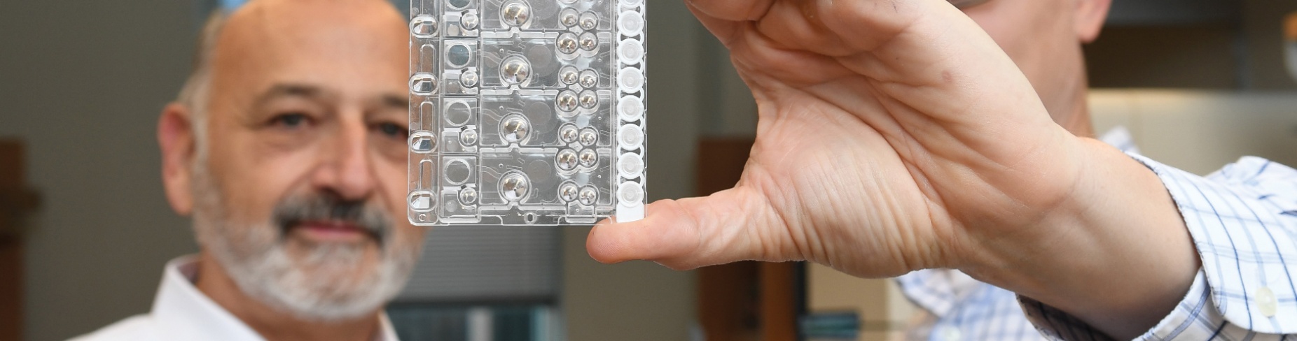 Richard Montagna (left) views the Rheonix CARD (r) Cartridge held by UB&rsquo;s Michael Buck. 