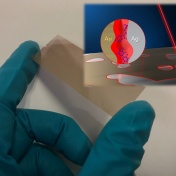 An illustration of the chip. A gloved hand holds a thin gold film which is struck by a beam of red light. An inset shows the chemical element abbreviations for gold and silver and the particles illuminated by the light. 