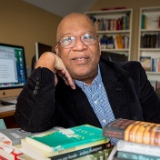 UB transnational studies professor Cecil Foster leaning on a stack of books on his desk. 