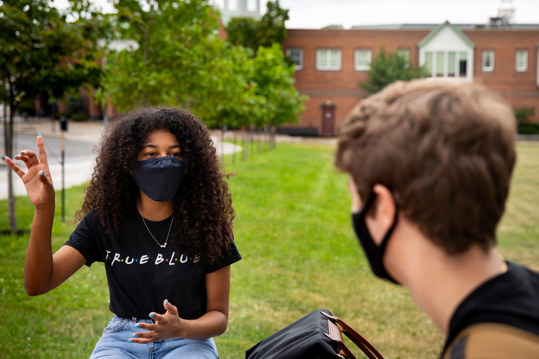 Two students talking while physically distanced and wearing face masks. 