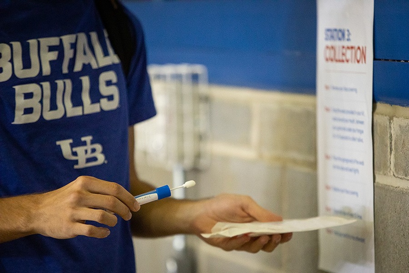 Student wearing a Bulls T-shirt prepares to take a saliva test. 