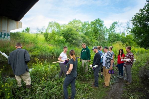 Zoom image: Kimberly Meehan (in white T-shirt and gray pants), UB clinical assistant professor of geology, speaks with teachers in the EarthEd Institute. The group journeyed to Bizer Creek on UB&rsquo;s North Campus on July 12 to collect sediment cores, which they later analyzed in the lab. Credit: Douglas Levere / University at Buffalo 