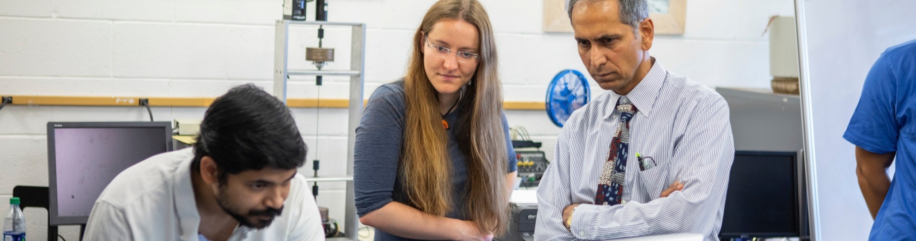 Two students look at a computer in the lab of UB professor Tarunraj Singh, who looks on. 