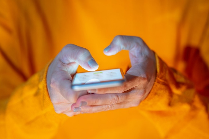 Person wearing orange shirt holding cell phone in hands. 