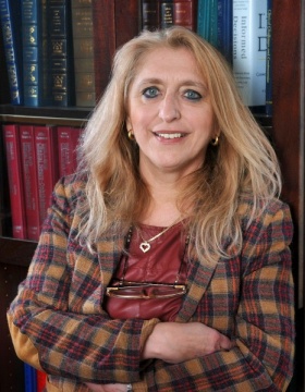 Bianca Weinstock-Guttman, arms folded, standing in front of bookshelf. 