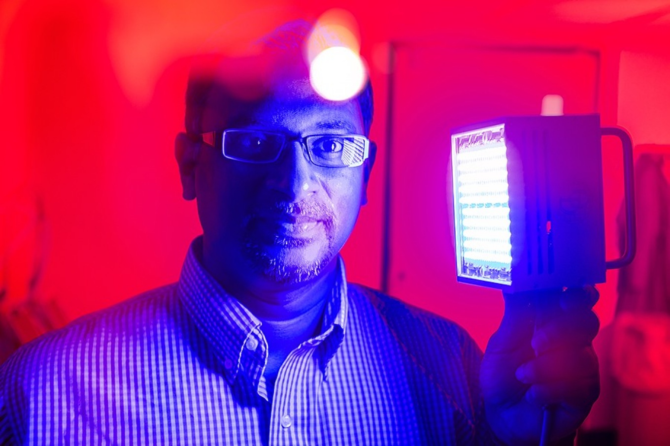 Portrait of oral biologist Praveen Arany, who is holding a device that emits low doses of light in a process known as photobiomodulation therapy. 