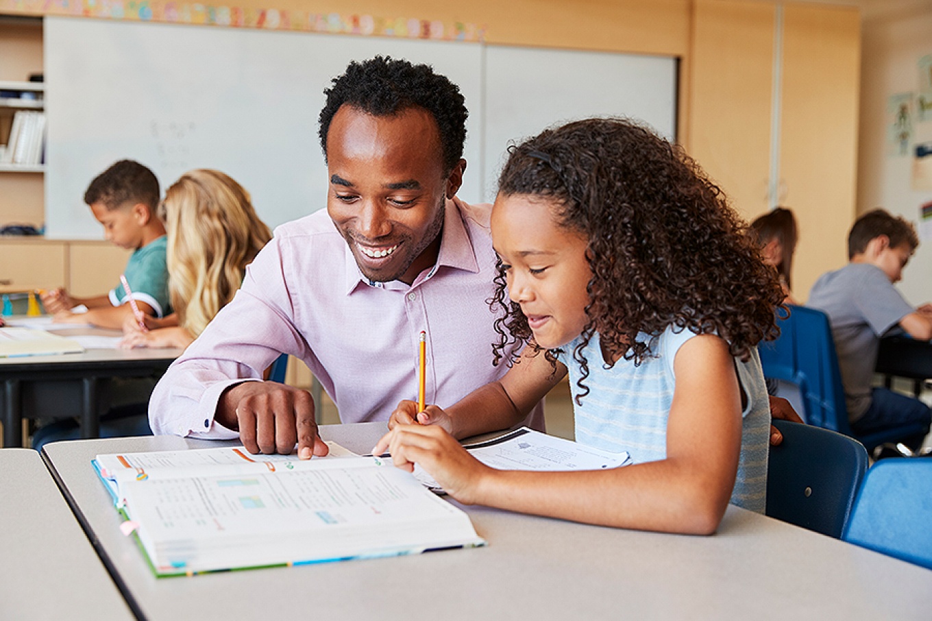A Black teacher and student work together in a classroom. 