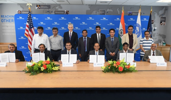 Participants of the UB-Indian Institutes of Technology UB-Indo Workshop sit and stand near a table with holding signed memorandum of understanding documents. 