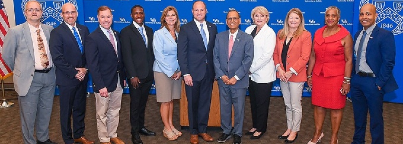 A group of university leaders and elected officials pose in a semi-circle. 