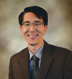 Portrait of a man wearing a dark suit, tie and glasses. 