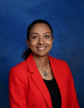 Smiling woman wearing a black shirt and red blazer in front of a blue background. 
