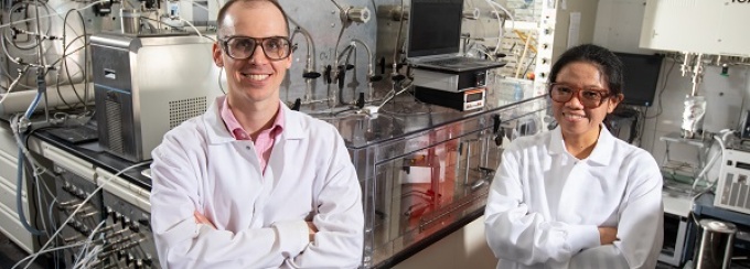 Tim Cook stands with arms crossed in his lab with student next to him. 
