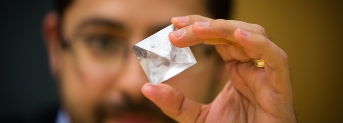 A man holds a diamond-shaped crystal in front of his face. 
