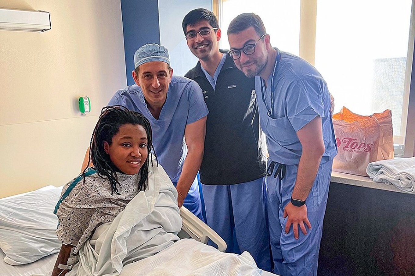 Zoom image: Sydney Johnson in the hospital just days after her surgery with her medical team led by Elad Levy (left), L. Nelson Hopkins Chair of Neurological Surgery in the Jacobs School of Medicine and Biomedical Sciences at UB and co-director of the Gates Stroke Center. Also pictured are Neil Almeida (center) and Justin Cappuzzo, both UB neurosurgery residents. 
