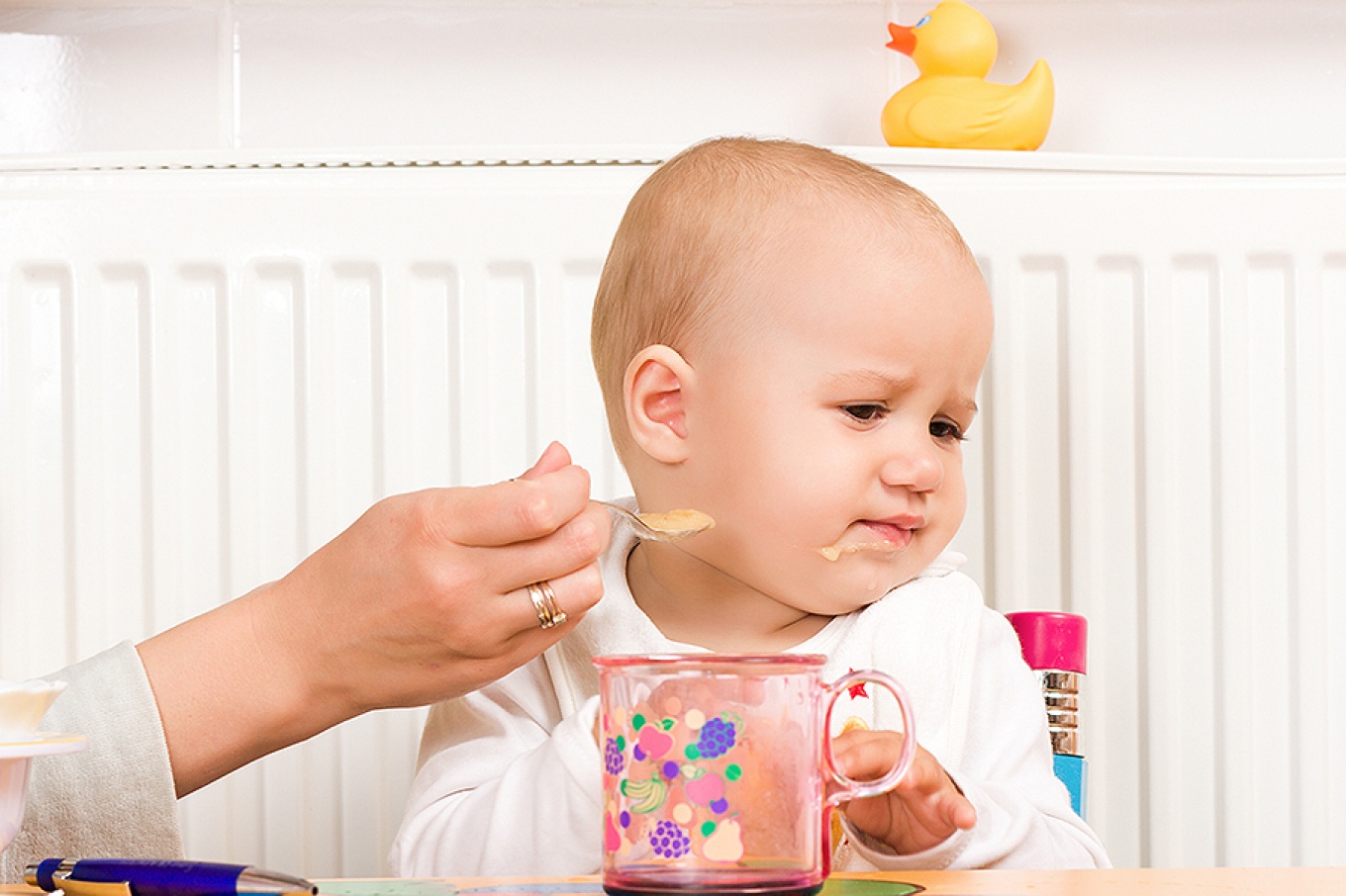 A baby make an unhappy face and turns away from baby food.