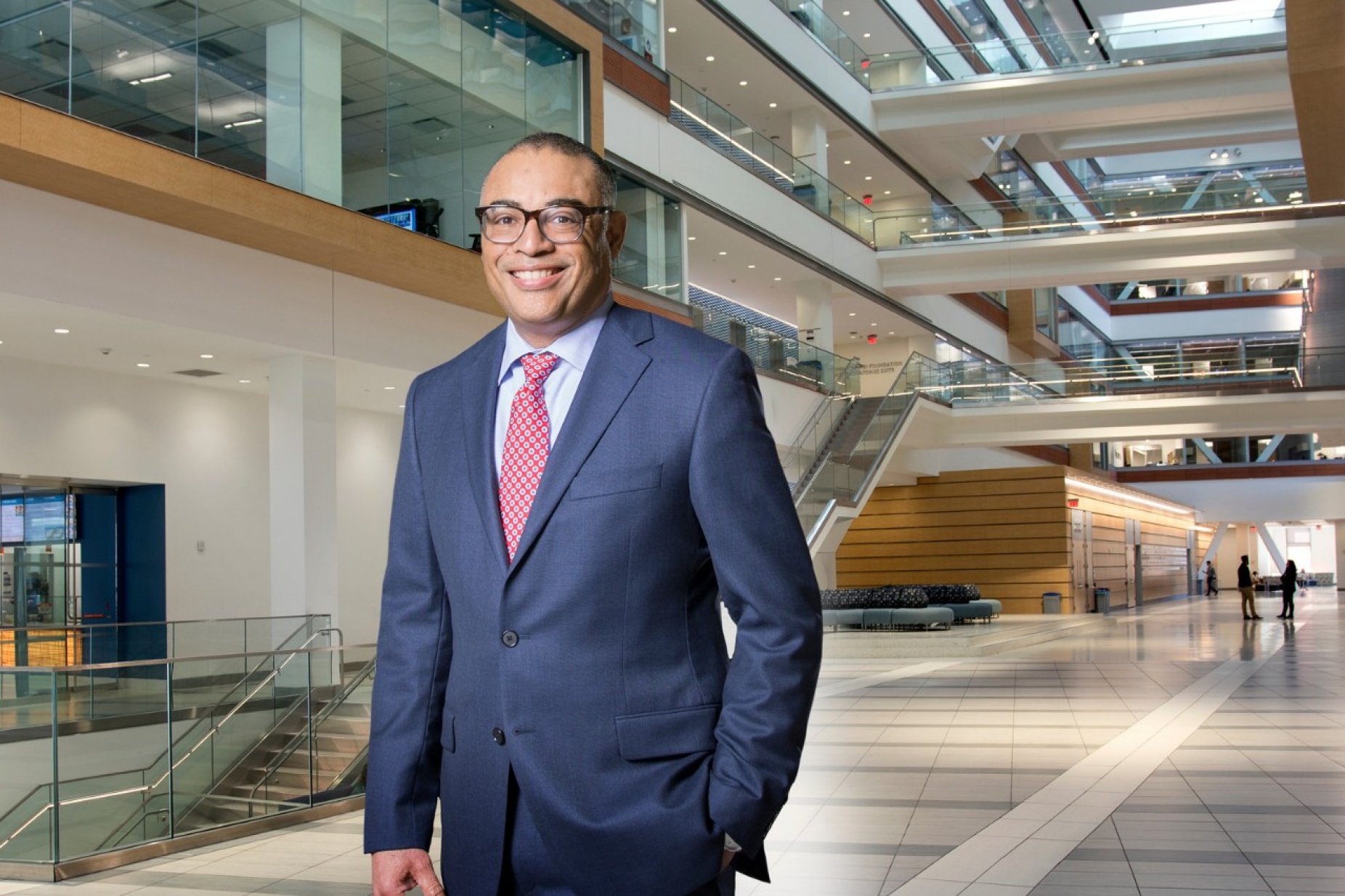 David Milling standing in med school atrium, wearing suit jacket and tie. 