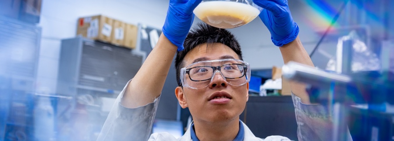 A scientist in Gang Wu's lab holds a glass globe above his head. 