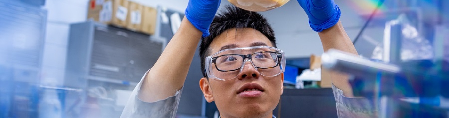 A scientist in Gang Wu's lab holds a glass globe above his head. 