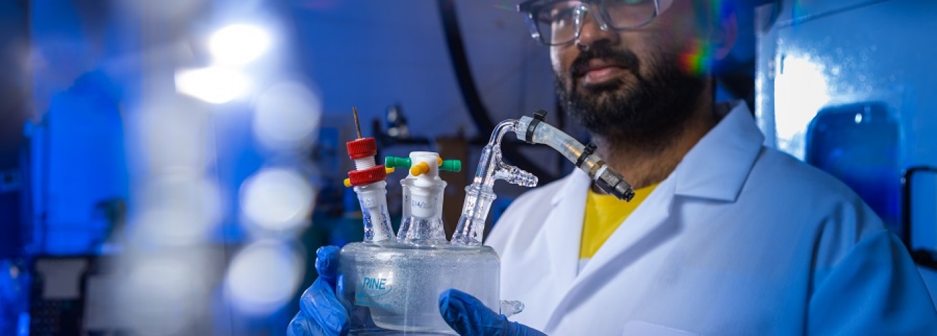 A student in Gang Wu's lab holds a glass object with tubes coming off it. 