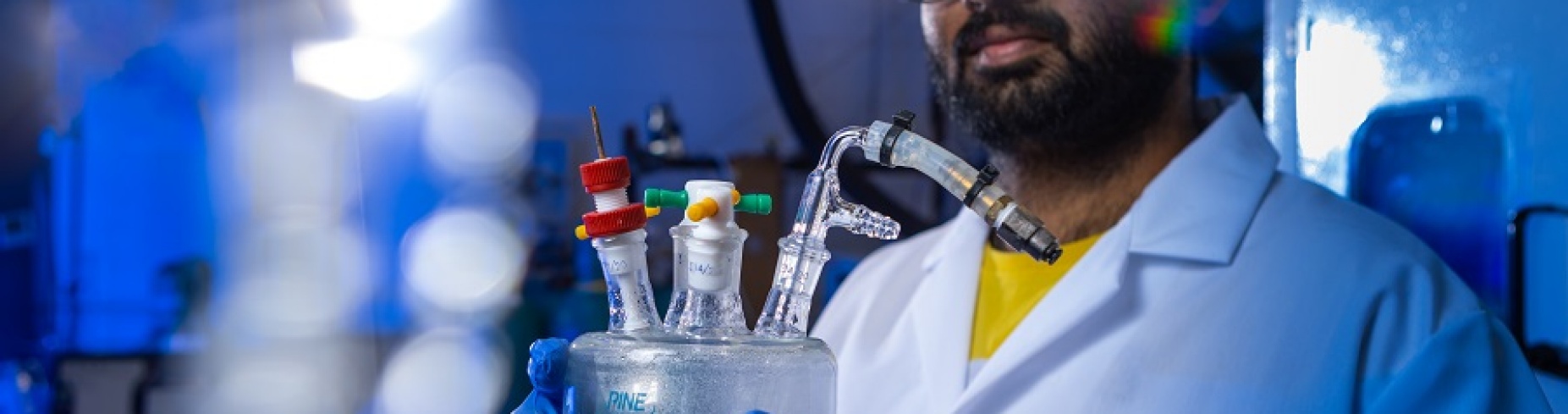 A student in Gang Wu's lab holds a glass object with tubes coming off it.