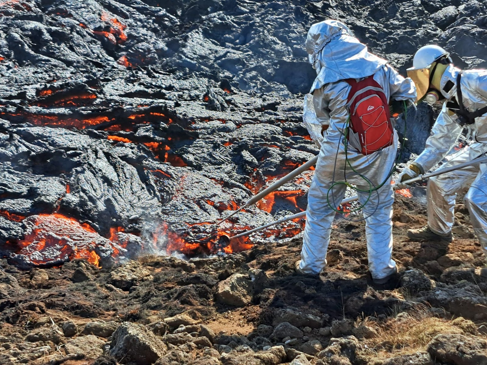 Researchers stand next to red hot lava to collect data on how its flowing Iceland. 