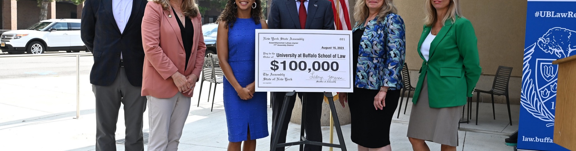 UB School of Law officials and state lawmakers stand in front of a large check for $100,000. 