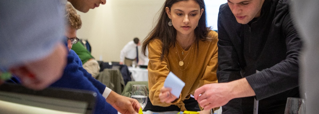 Students work hovering over a table with papers in their hands. 