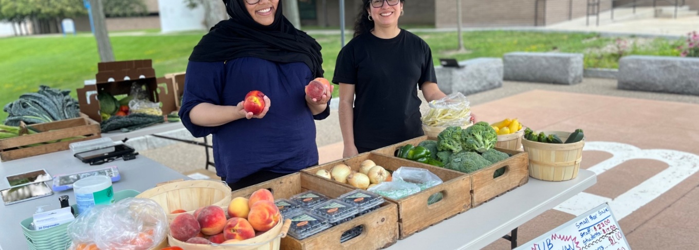 Two students displaying fresh produce at the UB Veggie Van mobile market. 