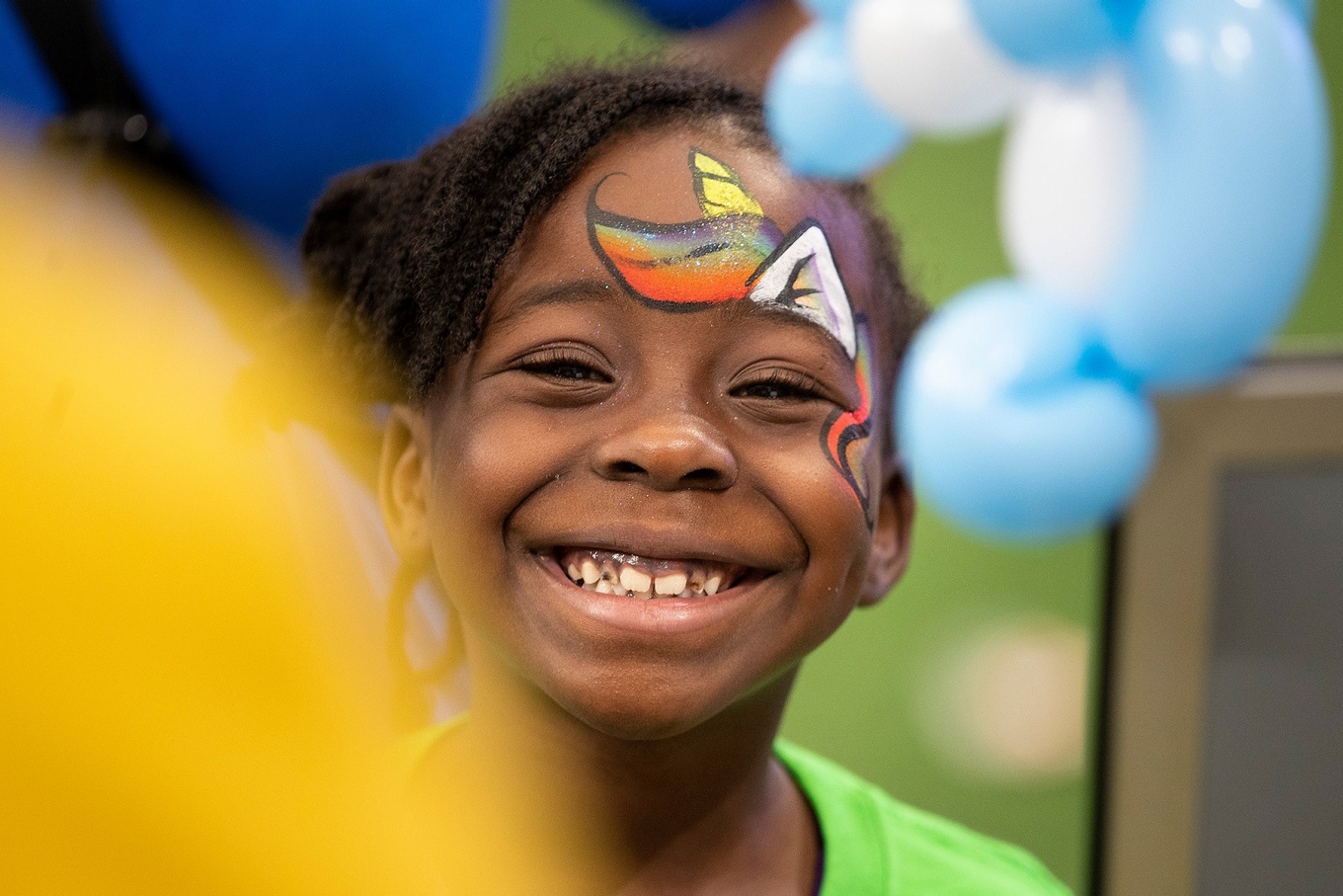 A young child surrounded by balloons smiles broadly. 