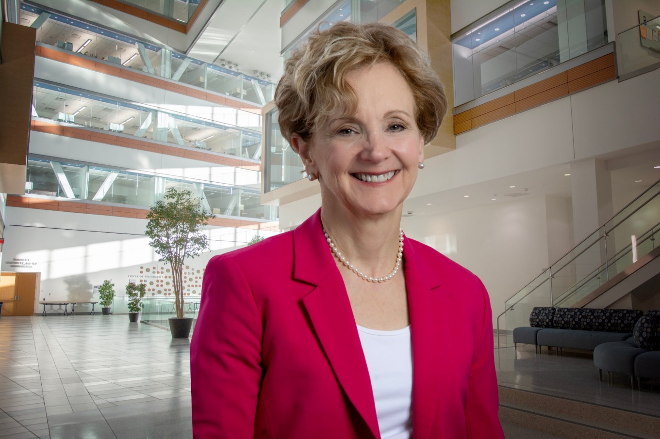 Allison Brashear, wearing a red blazer, is in the medical school atrium.