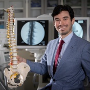 Esteban Quiceno is standing in a lab holding a skeleton of the spine. 