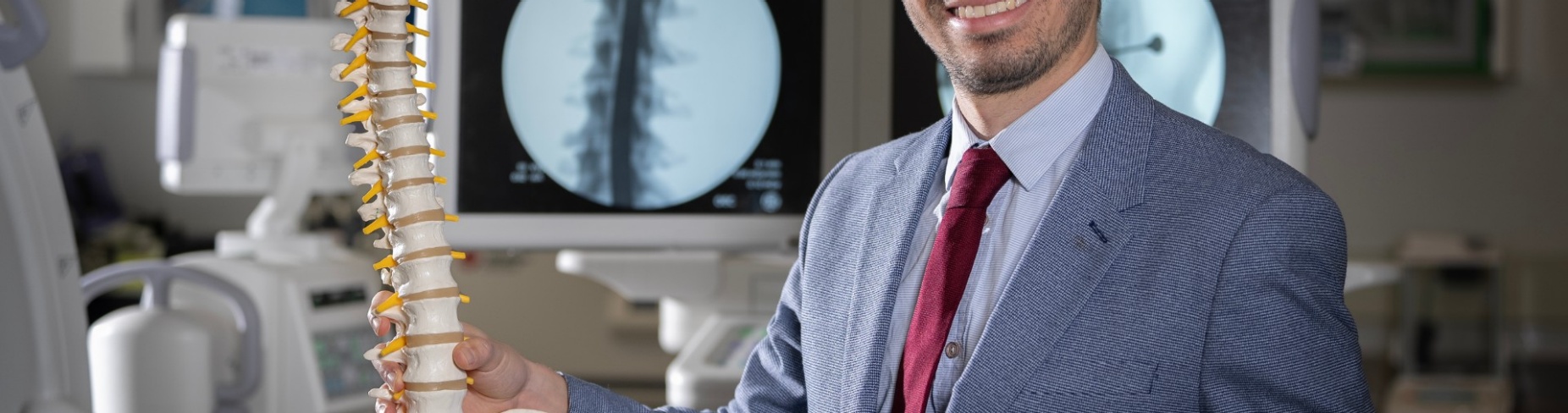 Esteban Quiceno is standing in a lab holding a skeleton of the spine. 