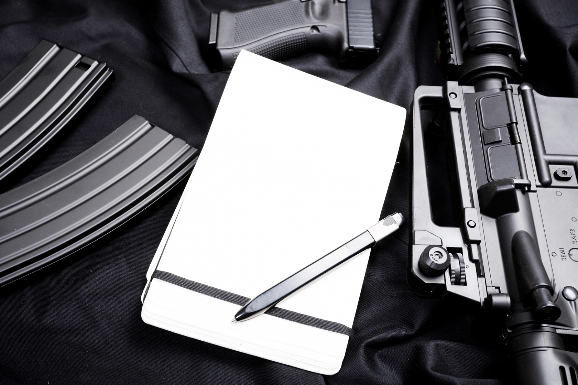 Guns and ammunition surrounding a notepad and pen. 