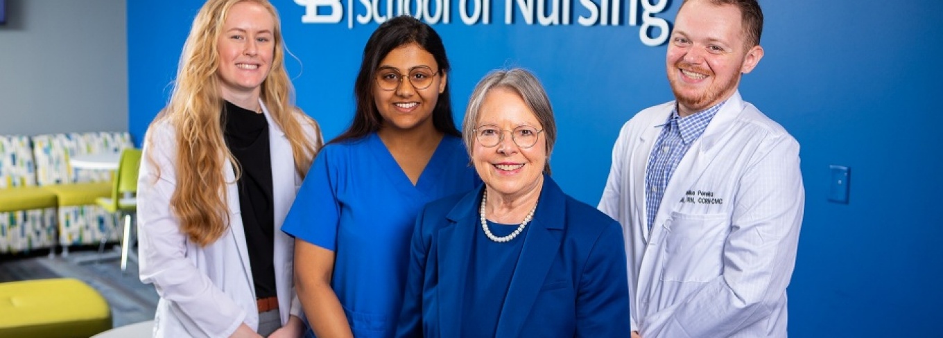 Annette Wysocki, dean of the School of Nursing, stands with three nursing students in front of a logo for the UB School of Nursing.