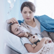 A young girl with an oxigen mask and a worried mother in a hospital room. 