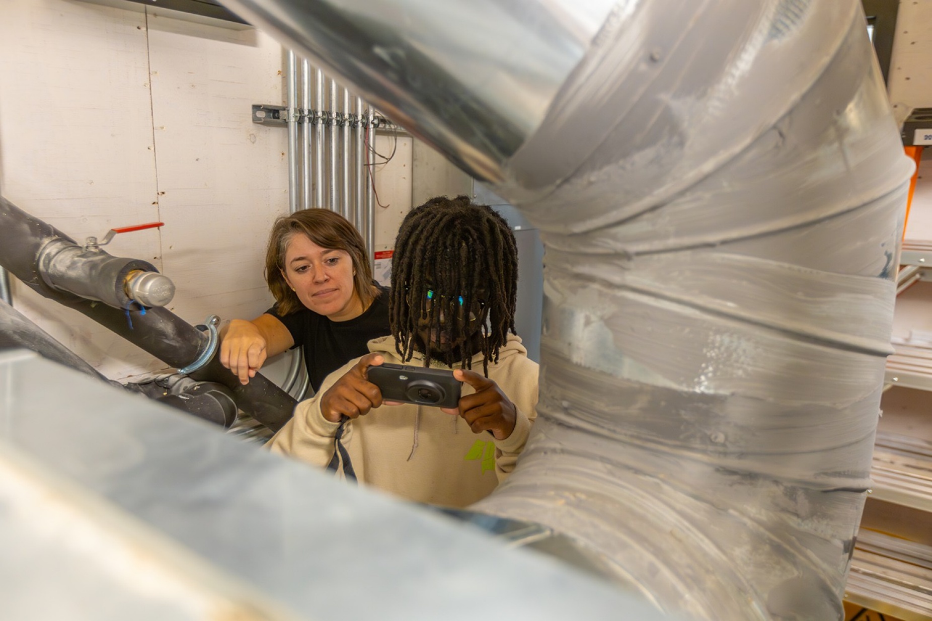 Female instructor watching as a male student points a small camera at a hot water tank. 