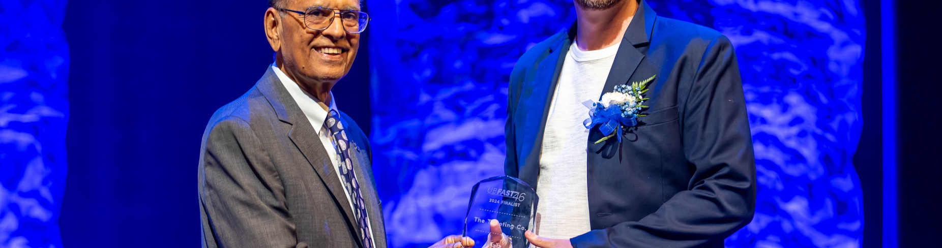 Satish Tripathi shakes hands with Trevor Titley while handing him an award.