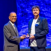 Satish Tripathi shakes hands with Trevor Titley while handing him an award. 