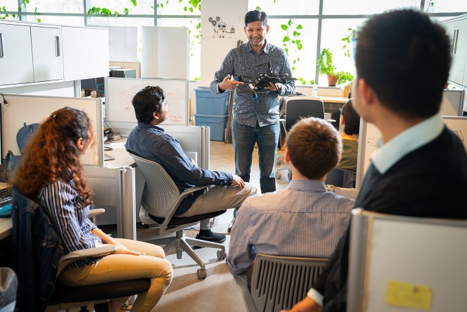 UB faculty member Karthik Dantu (center), who teaches in the UB Master of Science Program in AI, speaks to students in a lab while holding a drone. 