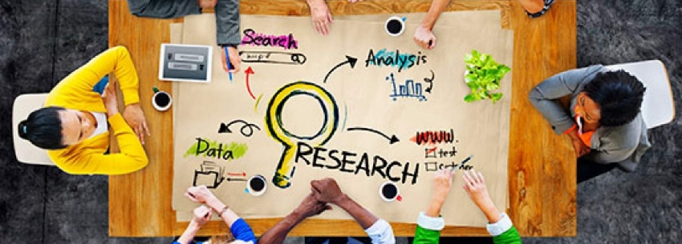 Image of people sitting at a big table collaborating on research ideas and topics. 
