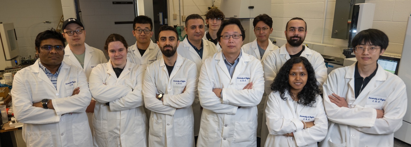 Miao Yu's lab group - about 15 people - stand together in white lab coats wit their arms folded.